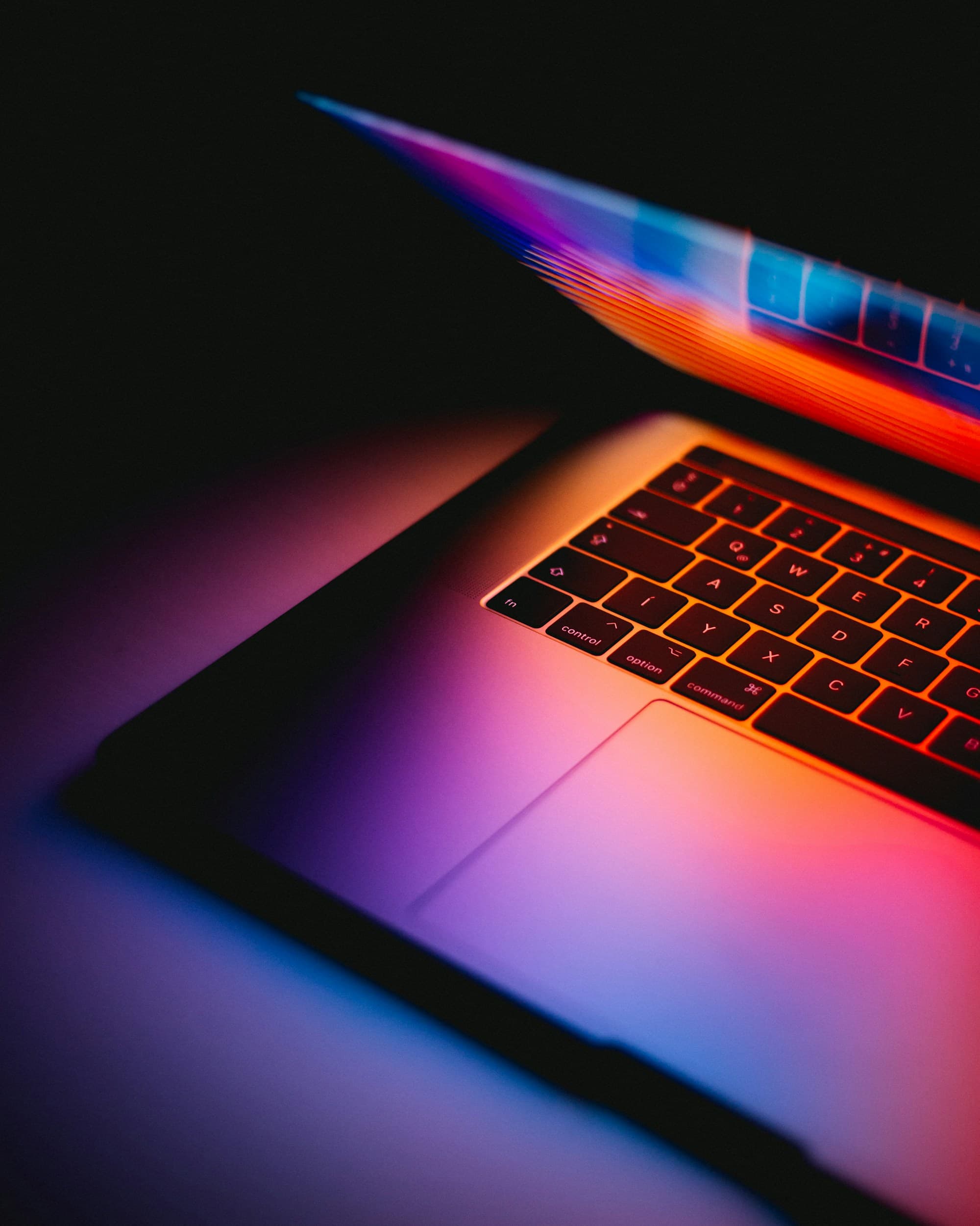 Laptop glowing with neon light in a dark workspace